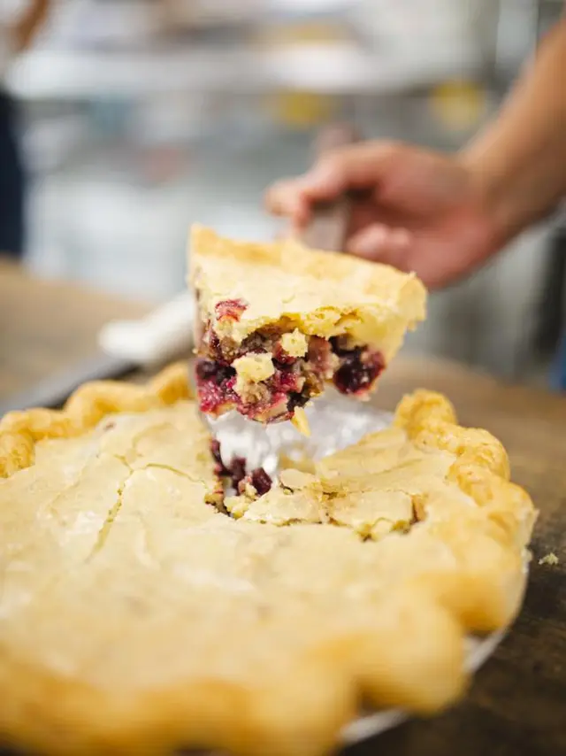 A hand lifting a piece of pie from the pie pan