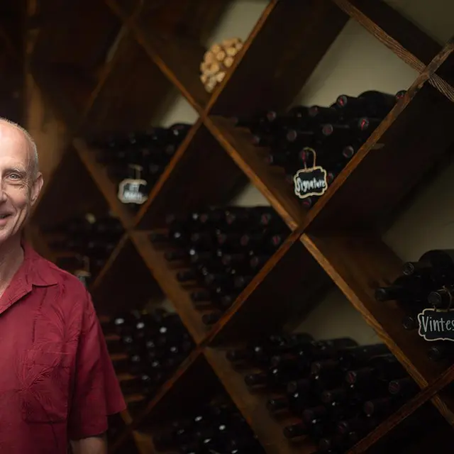 bald man standing in front of wall of shelves filled with wine bottles