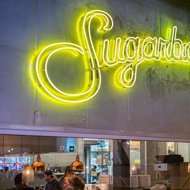 Yellow script neon Sugarbacon sign over kitchen opening