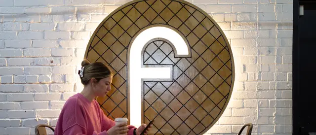 young woman at a table with coffee in hand looking at her phone