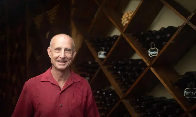 bald man standing in front of wall of shelves filled with wine bottles