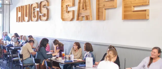 Hugs Cafe spelled out in wooden letters on wall with tables and customers beneath the sign