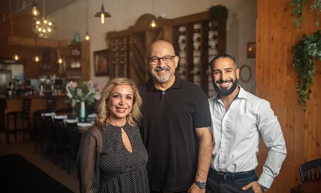 One woman and two men smiling and standing in front of a table in a restaurant