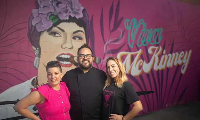 two women and man standing in front of a pink mural of a woman that says Viva McKinney