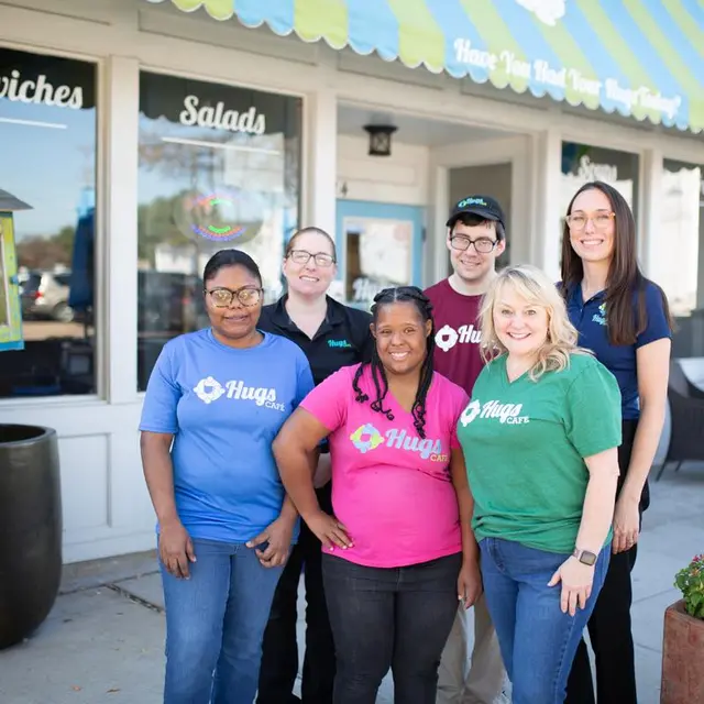 Diverse group of people wearing various colored Hugs tshirts in front of cafe