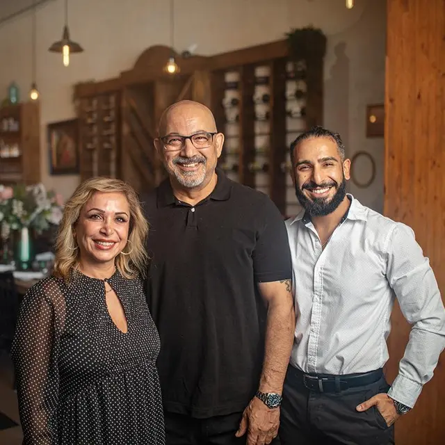 One woman and two men smiling and standing in front of a table in a restaurant