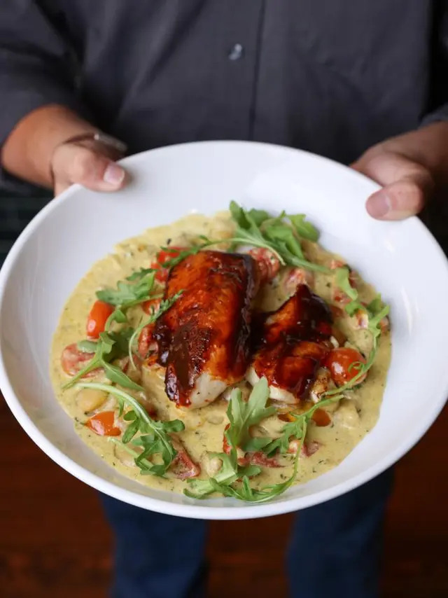 hands holding a white plate with sauce and a piece of chicken on top