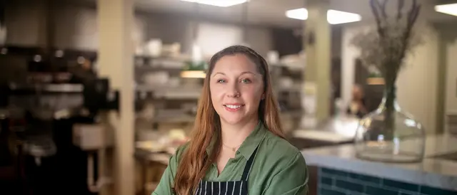young woman in a green blouse and black and white striped apron standing in a restaurant kitchen