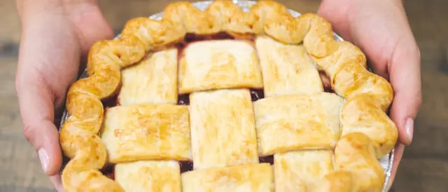 hands holding a large lattice-work crust topped pie