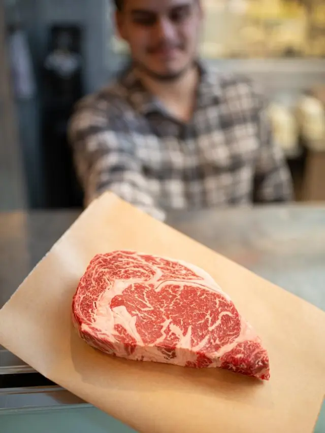 marbeled steak being handed toward camera