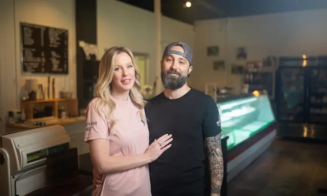 blonde woman in pink shirt with bearded man in black tshirt and tattooed arms in from of meat case