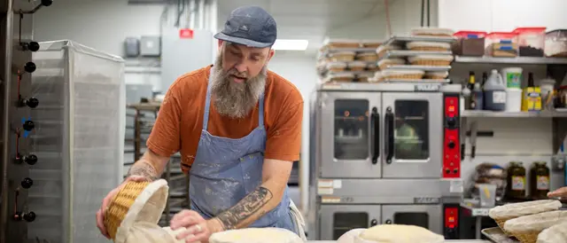 Bearded man in blue apron making bread