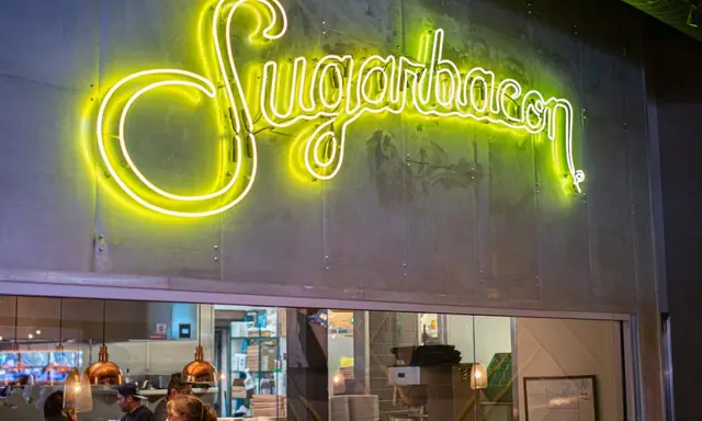 Yellow script neon Sugarbacon sign over kitchen opening