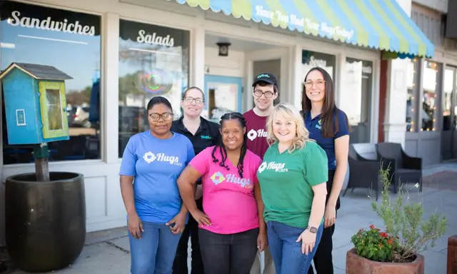 Diverse group of people wearing various colored Hugs tshirts in front of cafe