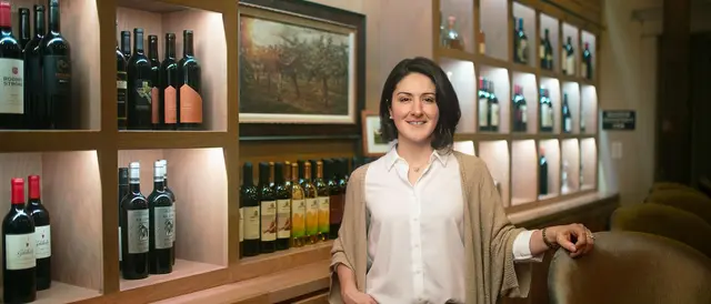Young brunette woman standing in bar with wine bottles on shelves behind her