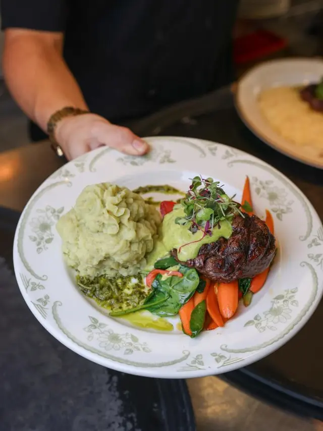 plate with mashed potatoes, steak covered in a green sauce, and fresh vegetables