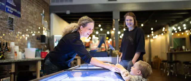 Woman leaning over the ice cream counter handing a cup of ice cream to a small child