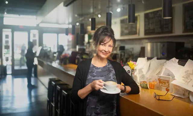 A smiling brunette woman standing at a counter holding a coffee cup