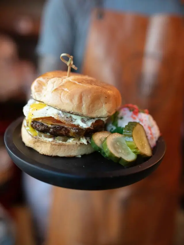 a black plate with a hamburger and pickle slices