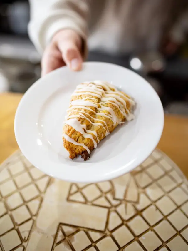 an iced scone on a plate that a hand it holding